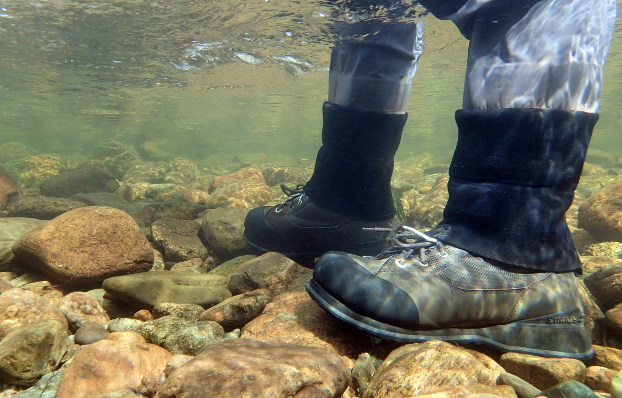 person stands in river with waders and wading boots on a rocky bottom