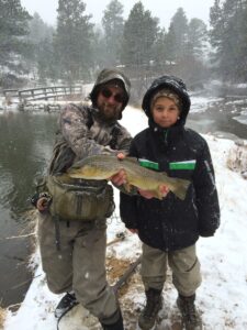 Man and kid hold a large brown trout while winter fly fishing in Colorado