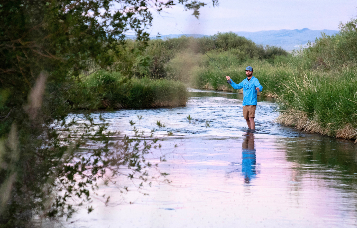 man in blue shirt casts a fly rod on a stream in Montana