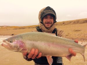 Man holds a large rainbow trout while winter fly fishing