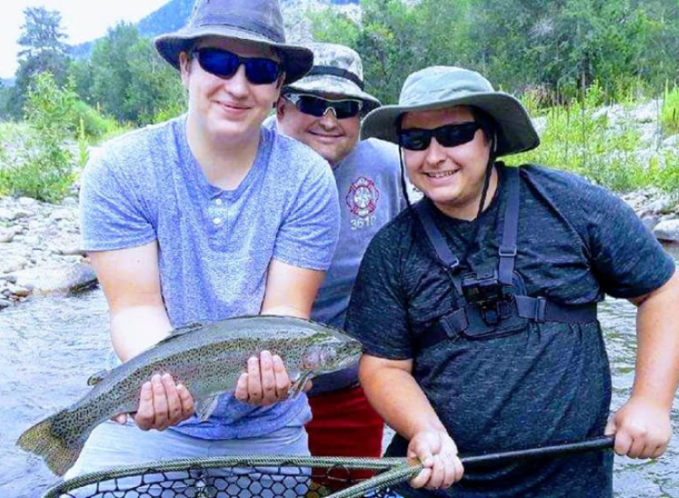 Three men with sunglasses on hold a rainbow trout
