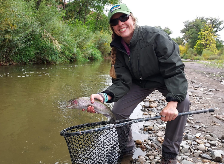 women holds rainbow trout and net while fly fishing