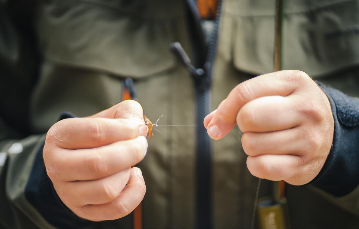 a man ties a knot in fishing line while fly fishing