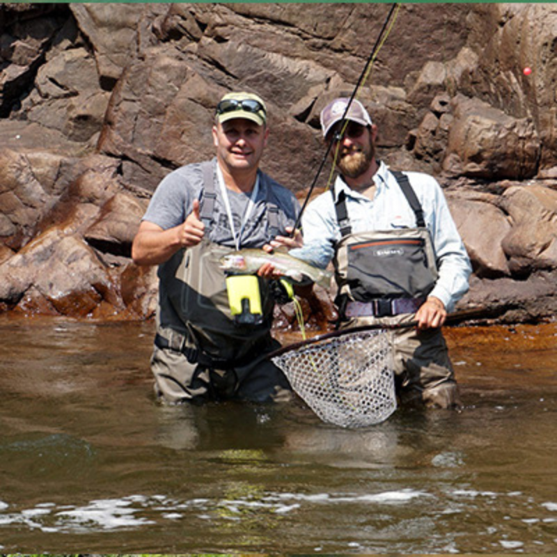 Two anglers stand in a river holding a rainbow trout while fly fishing