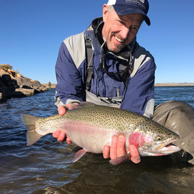 man holds a large rainbow trout while fly fishing in colorado