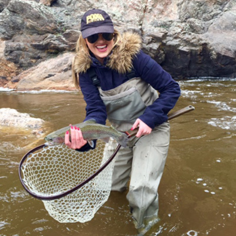 Woman holds rainbow trout while standing in a tea stained river and fly fishing in Colorado