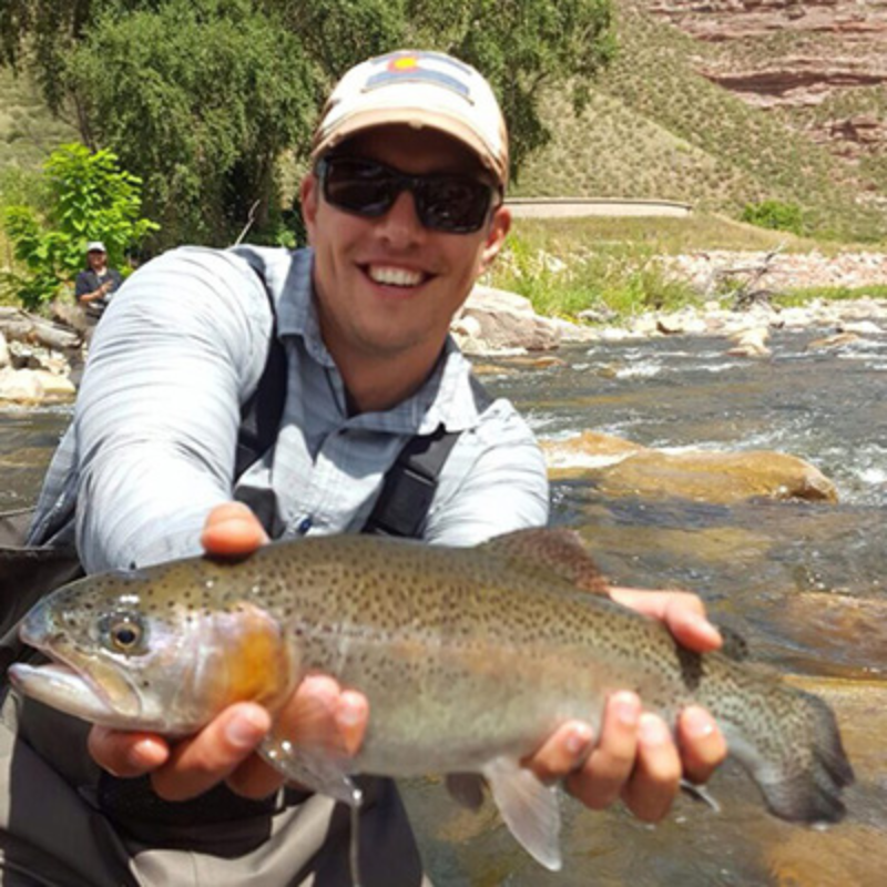 Man holds large rainbow trout above river while fly fishing in Colorado