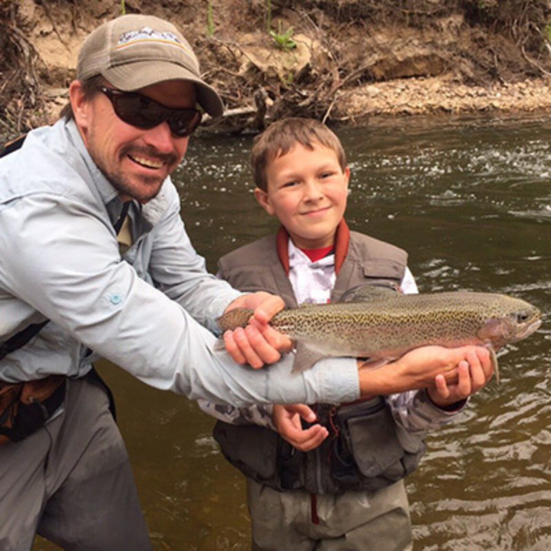 Man holds rainbow trout in front of kid while fly fishing in Colorado