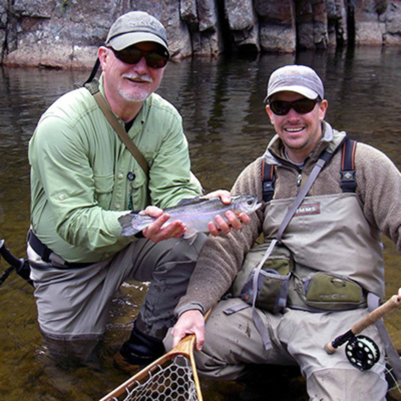 two anglers hold a rainbow trout while fly fishing in Colorado