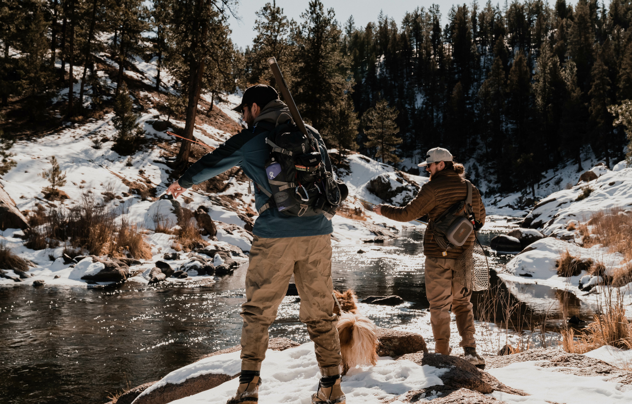 two men and a dog fly fish in the winter time in Colorado with snow on the banks