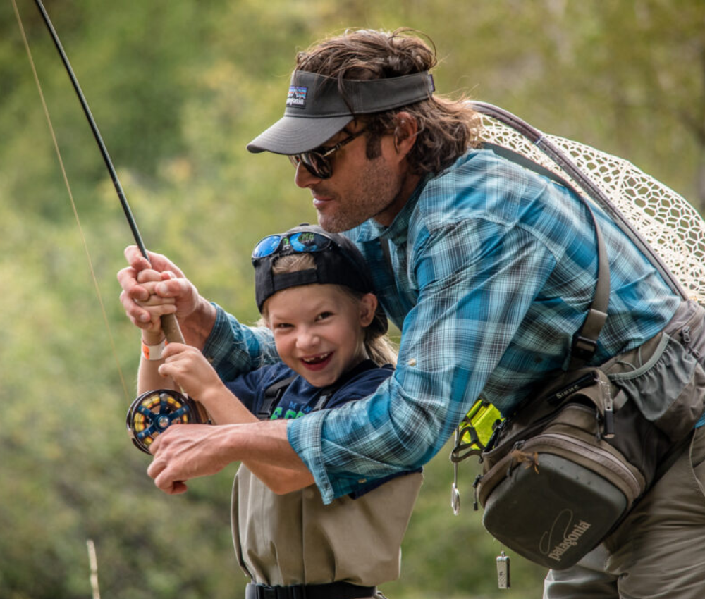 man helps a young child learn how to fly fish