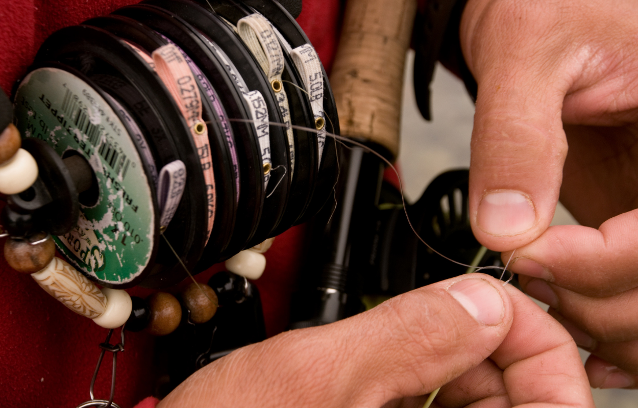 angler ties a knot in fishing line with a roll of fly fishing tippet