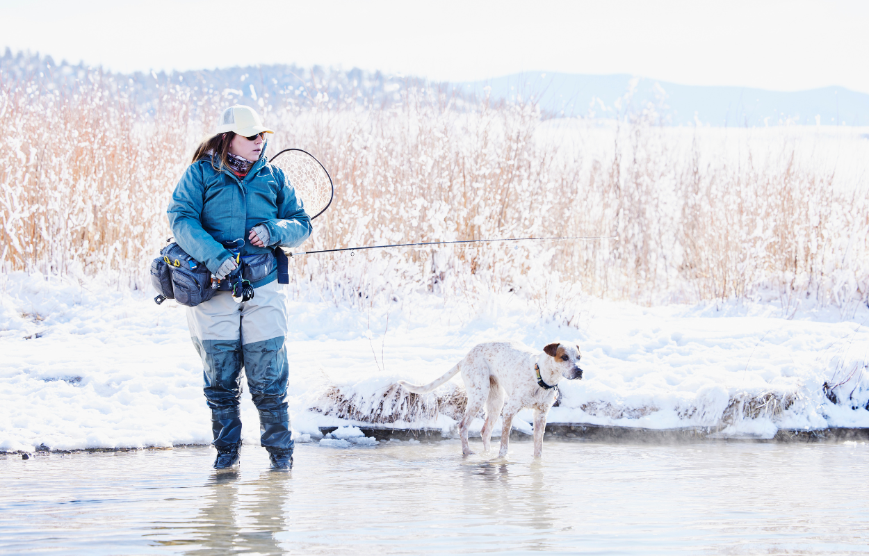 a women fly fishing with a white dog