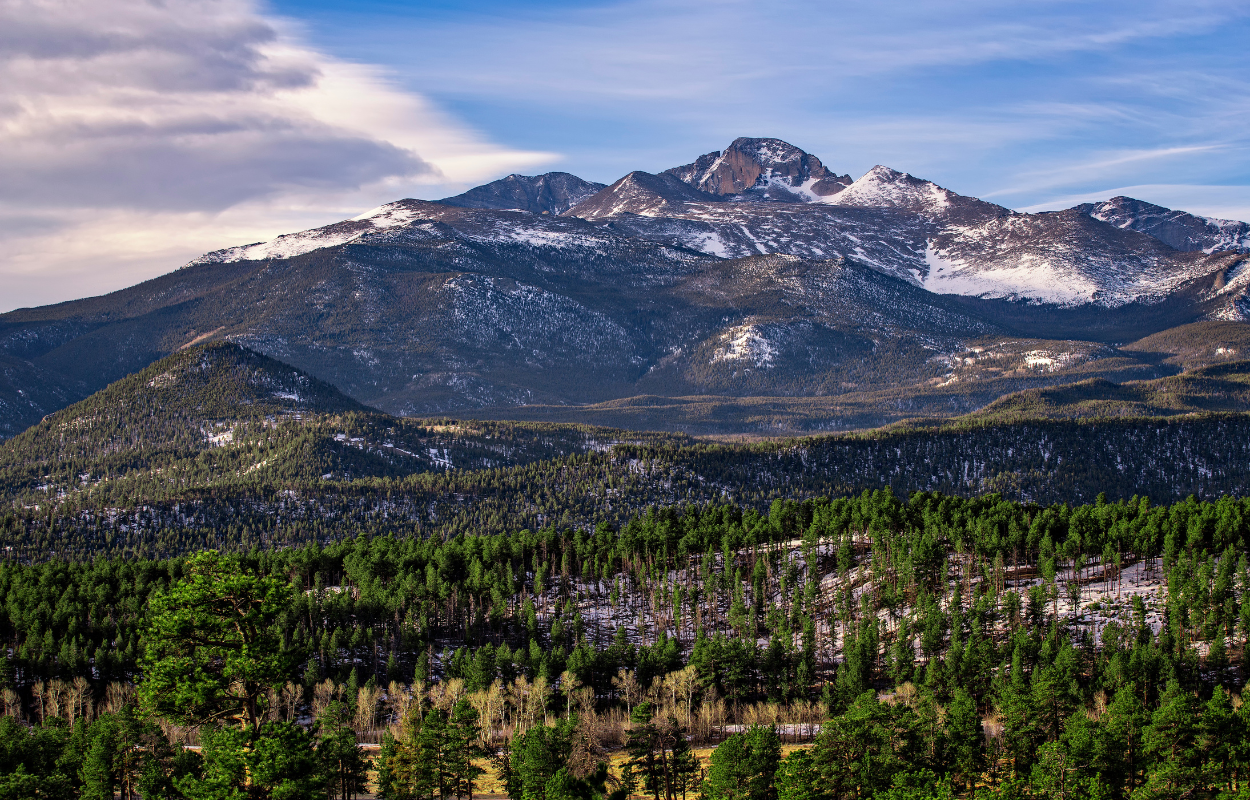 view of Longs Peak in Rocky Mountain National Park with a forested valley and light snowfall on the mountain